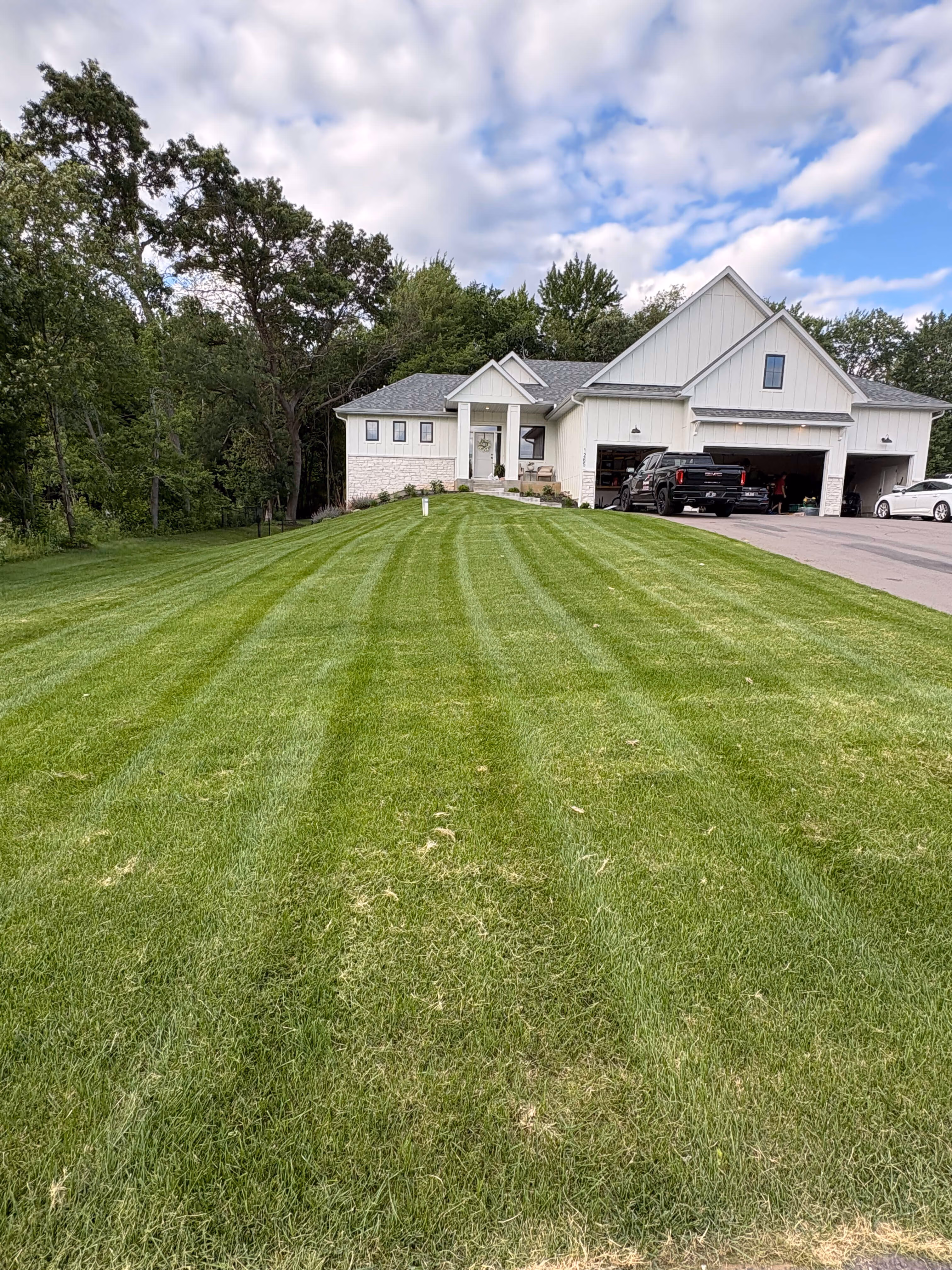 Front view of a white house with a large, freshly mowed green lawn and trees in the background.